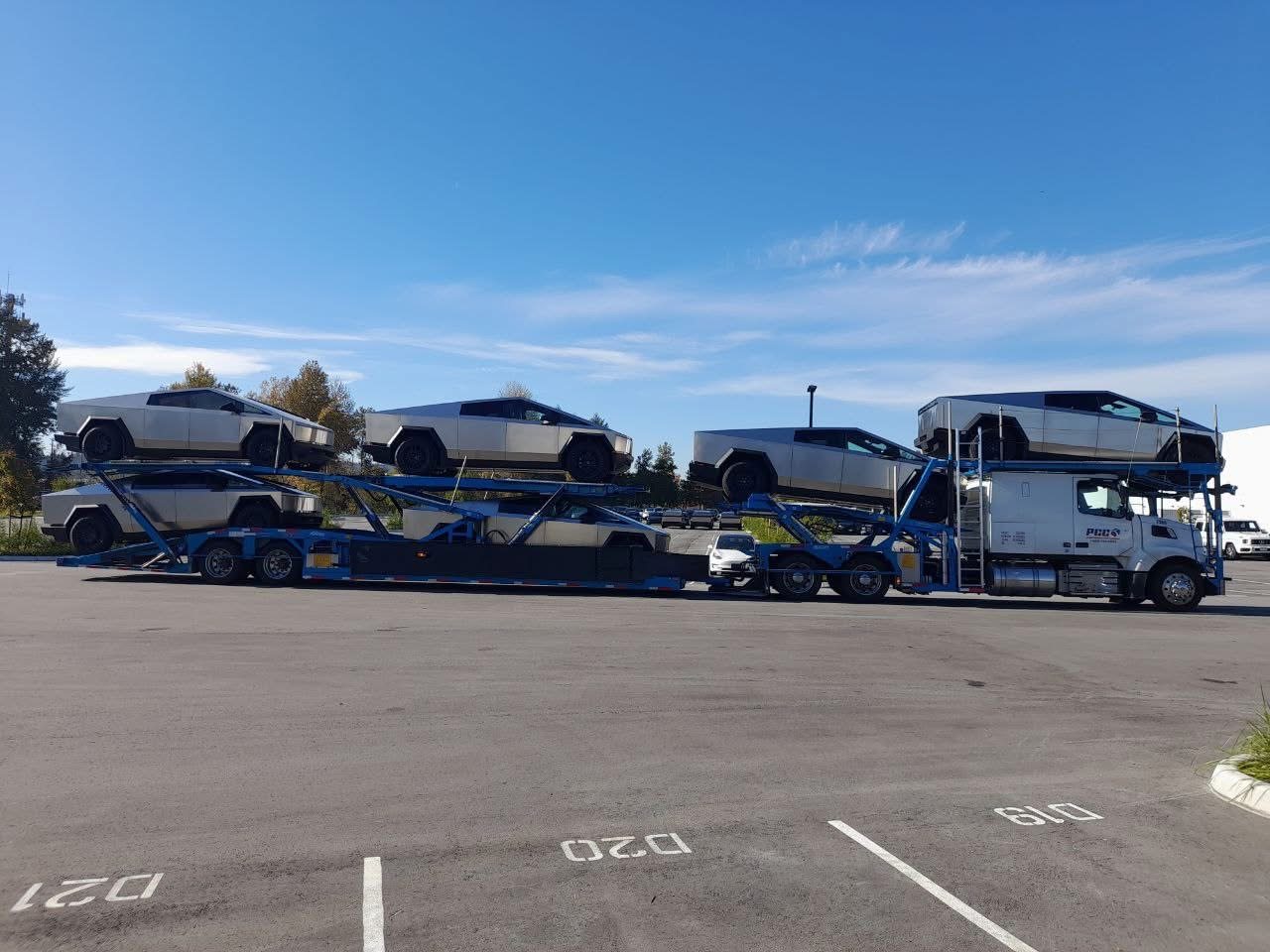 A car carrier loaded with four electric pickup trucks under a clear sky