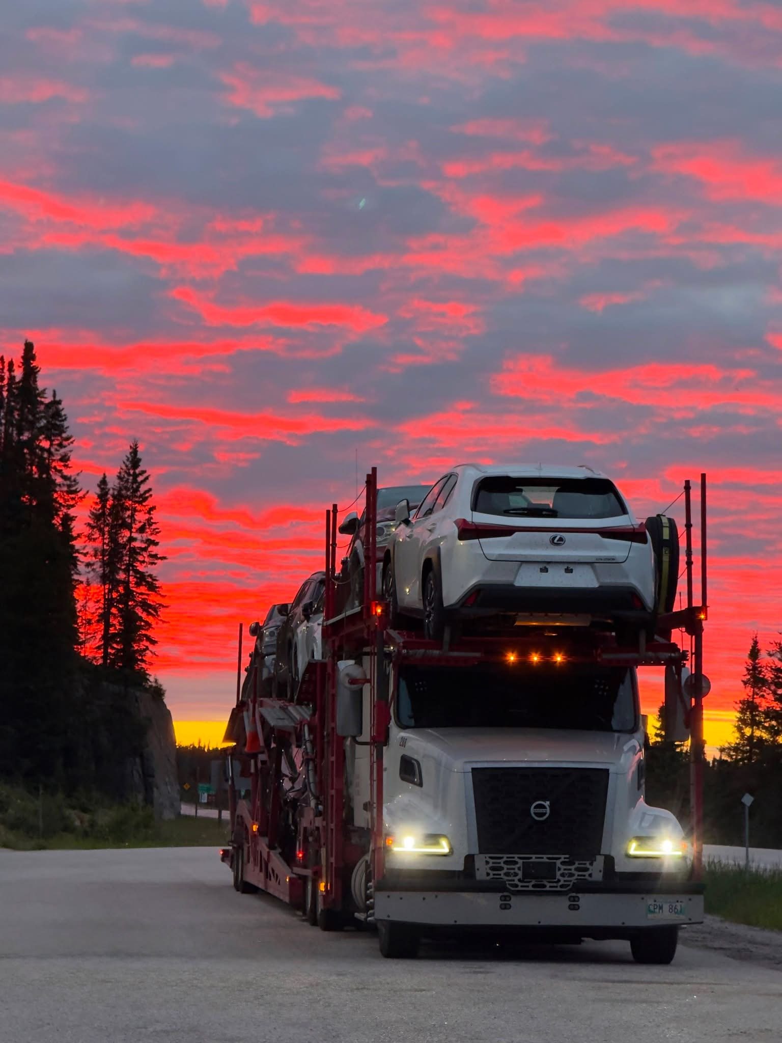 A loaded car carrier on the highway at sunset